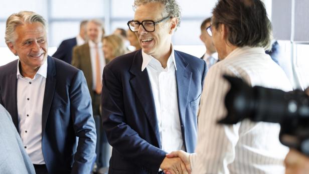 Mehrere Männer in Anzügen begrüßen sich freundlich per Handschlag in einem hellen Raum.
