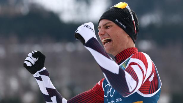 Ein jubelnder Skilangläufer mit Mütze und Handschuhen ballt die Fäuste.