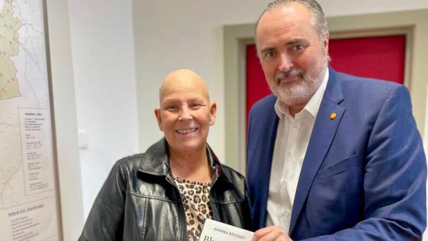 Zwei Personen stehen nebeneinander und halten gemeinsam ein Buch mit dem Titel „Blumen in der Wüste“.