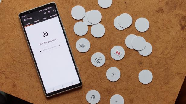 ein Smartphone mit der "NFC Tools" App, daneben weiße kreisrunde NFC-Tags