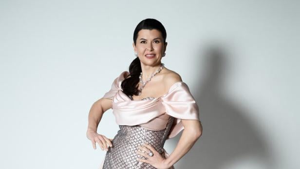 Frau mit dunklen Haaren trägt ein elegantes, bodenlanges Abendkleid in Rosa und Silber mit Muster und Schmuck.