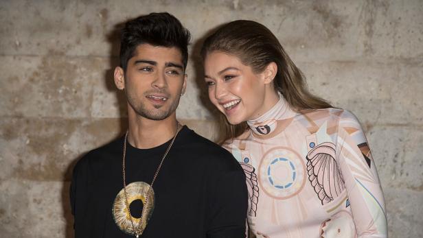 Zyan Malik und Gigi Hadid reden miteinander vor einer hellen Steinwand.