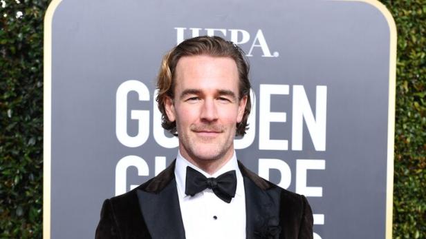 James Van Der Beek mit Fliege und Samtjackett posiert vor einem Golden Globes-Hintergrund.