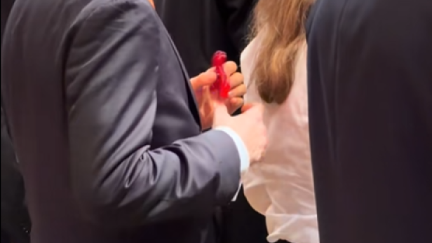 Ein junger Mann im Anzug dreht auf dem Opernball einen roten Fidget Spinner in der Hand.