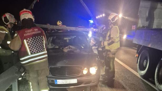Feuerwehrleute bergen nachts ein beschädigtes Auto auf der Autobahn mit einem Kran.