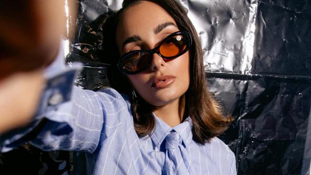 Influencerin Leandra Procelli trägt eine Sonnenbrille und posiert für die Kamera, Eine Hand hat sie dabei seitlich auf der Kameralinse