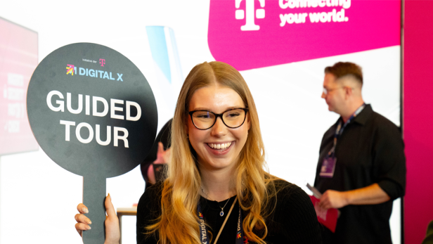 Junge Frau mit "Guided Tour"-Schild auf der DIGITAL X, im Hintergrund Messebesucher.