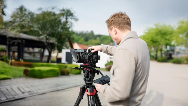 Mann bedient eine professionelle Videokamera auf einem Stativ im Freien.