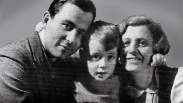 Ein Mann, ein Kind und eine Frau sitzen eng beieinander und lächeln gemeinsam in die Kamera.