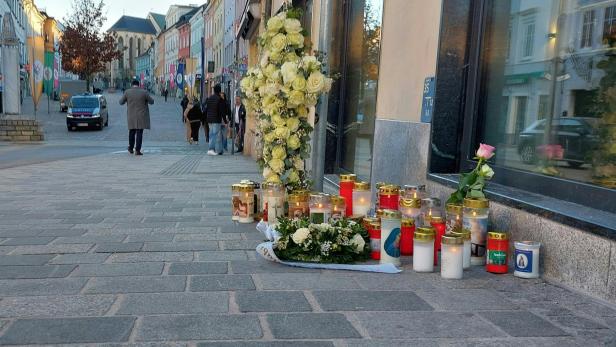 Kerzen, Blumen und ein Kreuz aus weißen Rosen stehen als Gedenkstätte auf einem Gehweg in Villach.