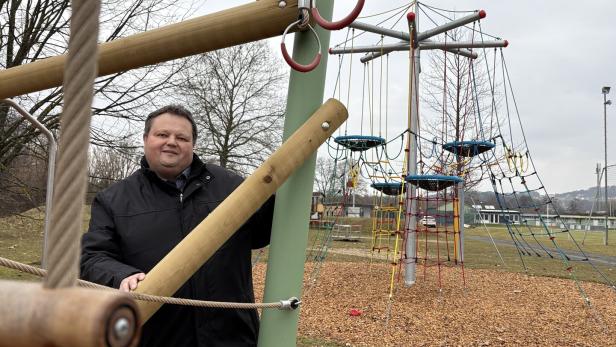 Ein Mann in Jacke steht auf einem Spielplatz mit Klettergerüsten.