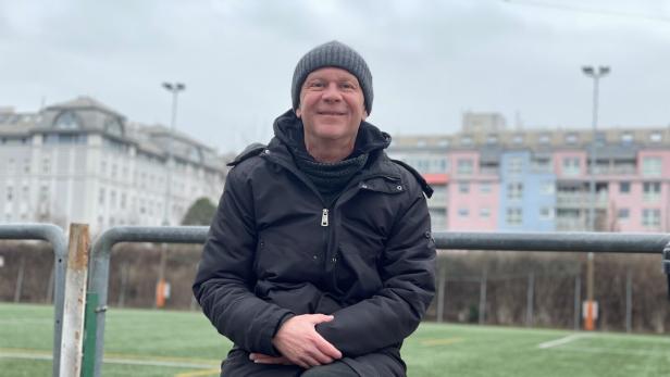 Helmut Emersberger sitzt auf einer Holzbank auf dem Sportplatz des WAT Brigittenau.