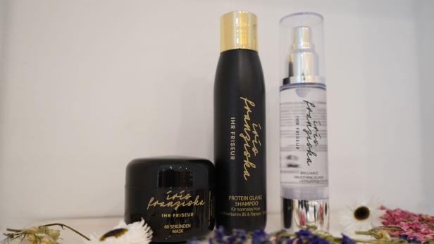 Drei Haarpflegeprodukte von Iris Franziska – Ihr Friseur, umgeben von Trockenblumen.