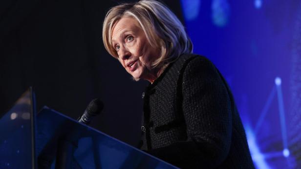 Hillary Clinton spricht an einem Rednerpult vor blauem Hintergrund.