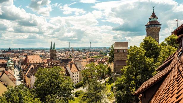 Blick über die Altstadt von Nürnberg mit historischen Gebäuden, Türmen und grünen Bäumen unter bewölktem Himmel