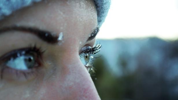 Nahaufnahme eines Gesichts mit gefrorenen Wimpern und Augenbrauen, die Person trägt eine Mütze.