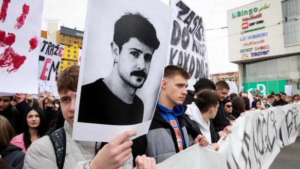 Demonstranten halten Schilder und ein Schwarzweiß-Porträt bei einer Kundgebung.