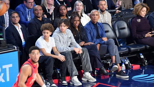 Michelle und Barack Obama sitzen mit anderen Zuschauende bei einem Basketballspiel. Tochter Sasha sitzt hinter ihnen.