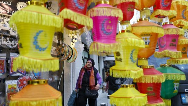 Bunte Laternen mit Fransen hängen über einer Frau, die durch eine belebte Straße mit Geschäften geht.
