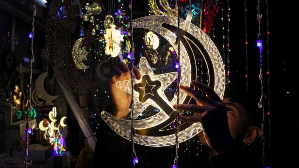 Eine Person hält eine leuchtende Dekoration in Form von Halbmond und Stern zwischen bunten Lichterketten.