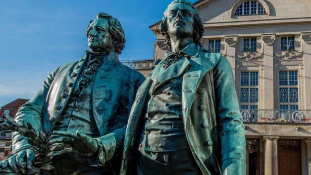 Zwei Statuen von Goethe und Schiller vor einem historischen Gebäude in Weimar.