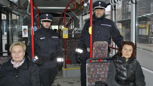 Zwei Polizisten stehen in einem Bus, während zwei ältere Damen sitzen.