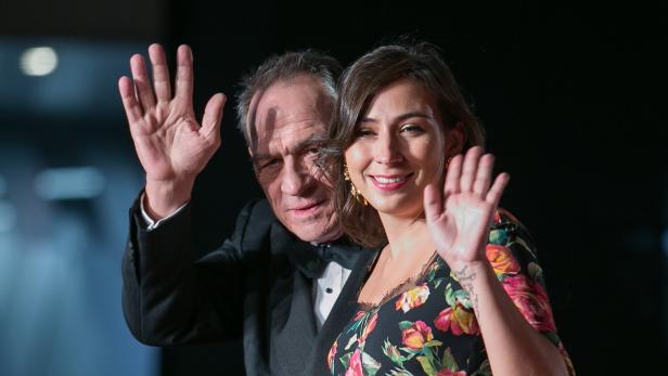 Tommy Lee Jones im Smoking und Victoria Jones im geblümten Kleid winken lächelnd in die Kamera.