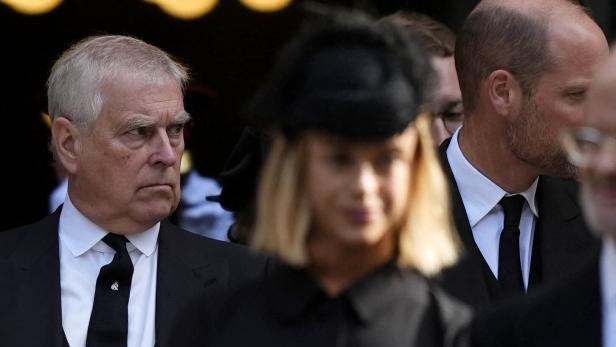 Ex-Prinz Andrew Mountbatten-Windsor und mehrere Personen in dunkler, formeller Kleidung. Sie stehen eng beieinander, einige tragen schwarze Hüte.