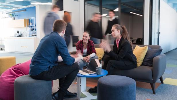 Multiethnic startup business team on meeting in a modern bright open space coworking office. Brainstorming, working on laptop. Group of coworkers walking around in motion blur.