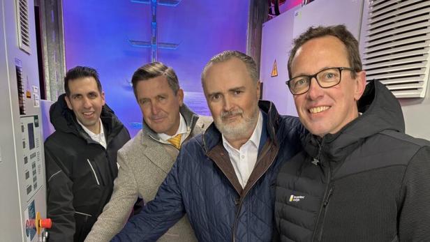 Vier Männer stehen in einem Raum mit technischer Ausrüstung und bedienen gemeinsam eine Steuerung.