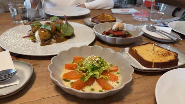 Eine Aufnahme von einem Esstisch auf dem mehrere Speisen stehen, darunter Lachs, Knödl und Brioche.