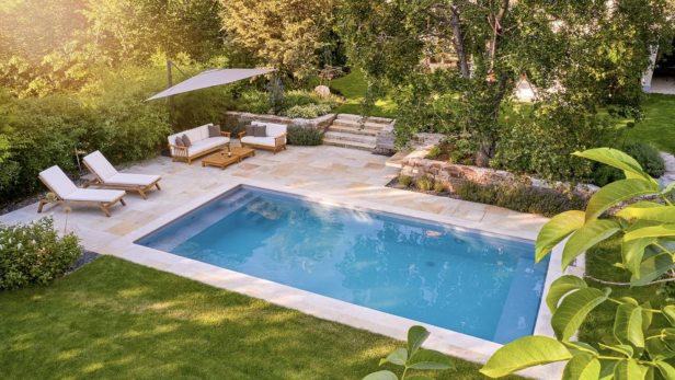 Ein Schwimmbecken im Garten mit einer Liege und einem Sonnenschirm.