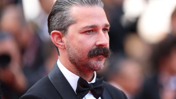 Shia LaBeouf mit zurückgekämmtem Haar und Schnurrbart trägt einen Smoking mit Fliege.