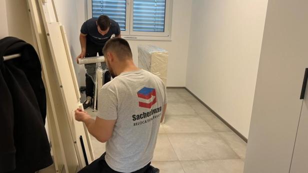 Zwei Männer von einer Umzugsfirma arbeiten in einem Raum und montieren Möbel ab.