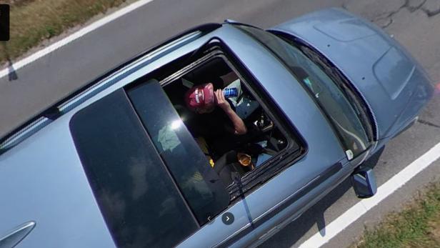 Mann trinkt Bier am Steuer eines Autos, aufgenommen durch das offene Schiebedach.