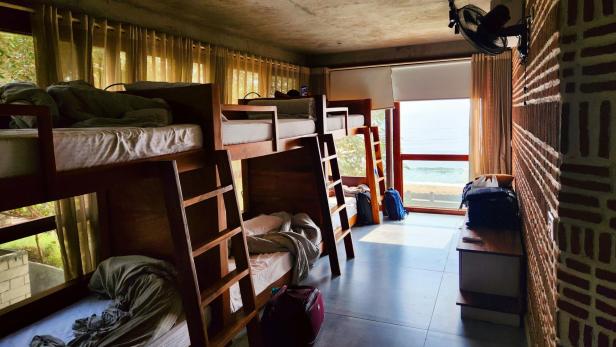 Mehrere Hochbetten in einem hellen Schlafraum mit Koffern und Blick auf einen See.