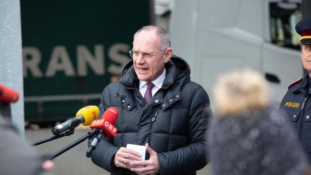Ein Mann spricht bei einer Pressekonferenz im Freien neben einem Polizisten.