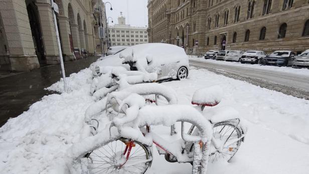Fahrräder und Autos sind von einer dicken Schneeschicht auf einer Stadtstraße bedeckt.