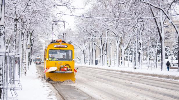 Eine gelbe Schneeräum-Straßenbahn fährt durch eine verschneite Stadt.