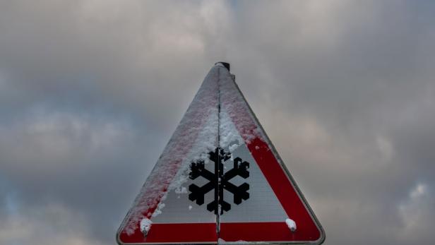 Ein dreieckiges Warnschild mit Schneeflockensymbol ist teilweise mit Schnee bedeckt.
