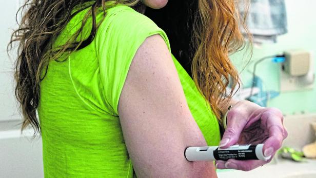 Eine Frau mit langen Haaren spritzt sich mit einem Injektionspen in den Oberarm.