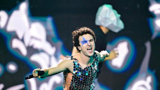 Ein Sänger mit blauem Stern im Gesicht performt mit glitzerndem Oberteil und Mikrofon auf der Bühne von Vienna Calling. 