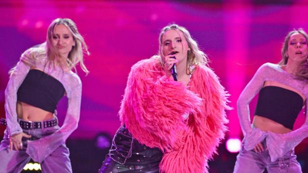Sängerin Julia Steen beim ESC-Vorentscheid Vienna Calling mit zwei Tänzerinnen auf einer Bühne mit pinkem Licht.
