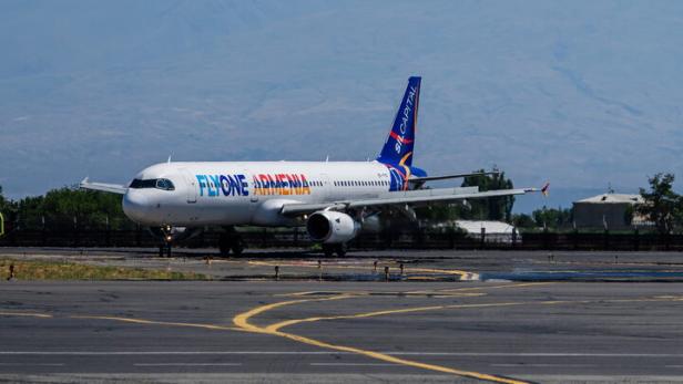 Ein Flugzeug von FlyOne Armenia steht vor einem schneebedeckten Berg auf einer Startbahn.