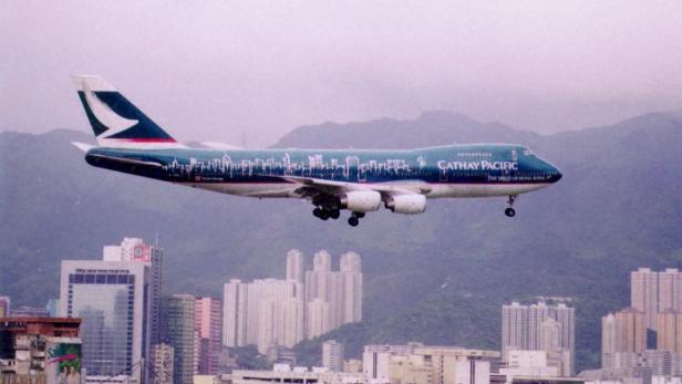 Flugzeug von Cathay Pacific im Landeanflug über Hochhäusern vor Bergen in Hongkong.