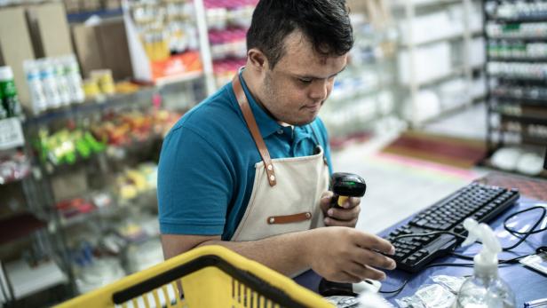 Mitarbeiter in einer Drogerie scannt Waren an der Kasse und tippt am Computer.