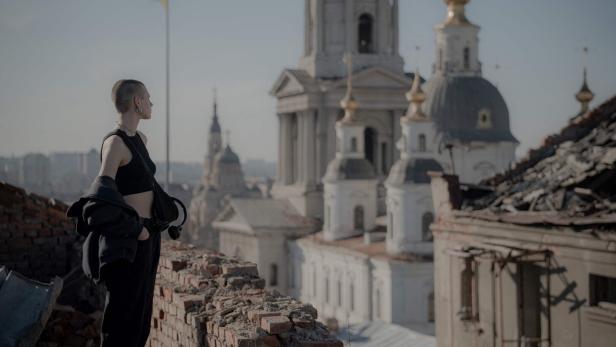 Eine Frau auf einem Dach schaut auf ein zerstörtes Gebäude