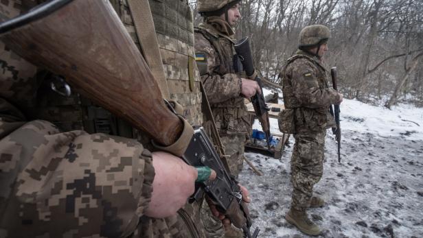 Drei Soldaten in Tarnuniform mit Gewehren stehen auf verschneitem Boden im Wald.
