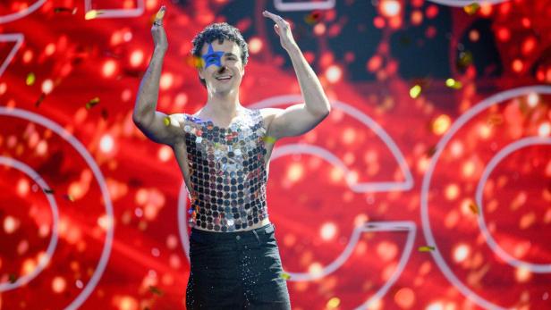 Cosmó jubelt auf der Bühne des ESC-Vorentscheids in glitzerndem Outfit vor rotem Hintergrund.