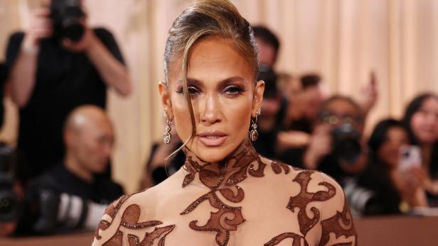 Jennifer Lopez posiert in einem verzierten Kleid mit hochgesteckten Haaren vor Kameras.